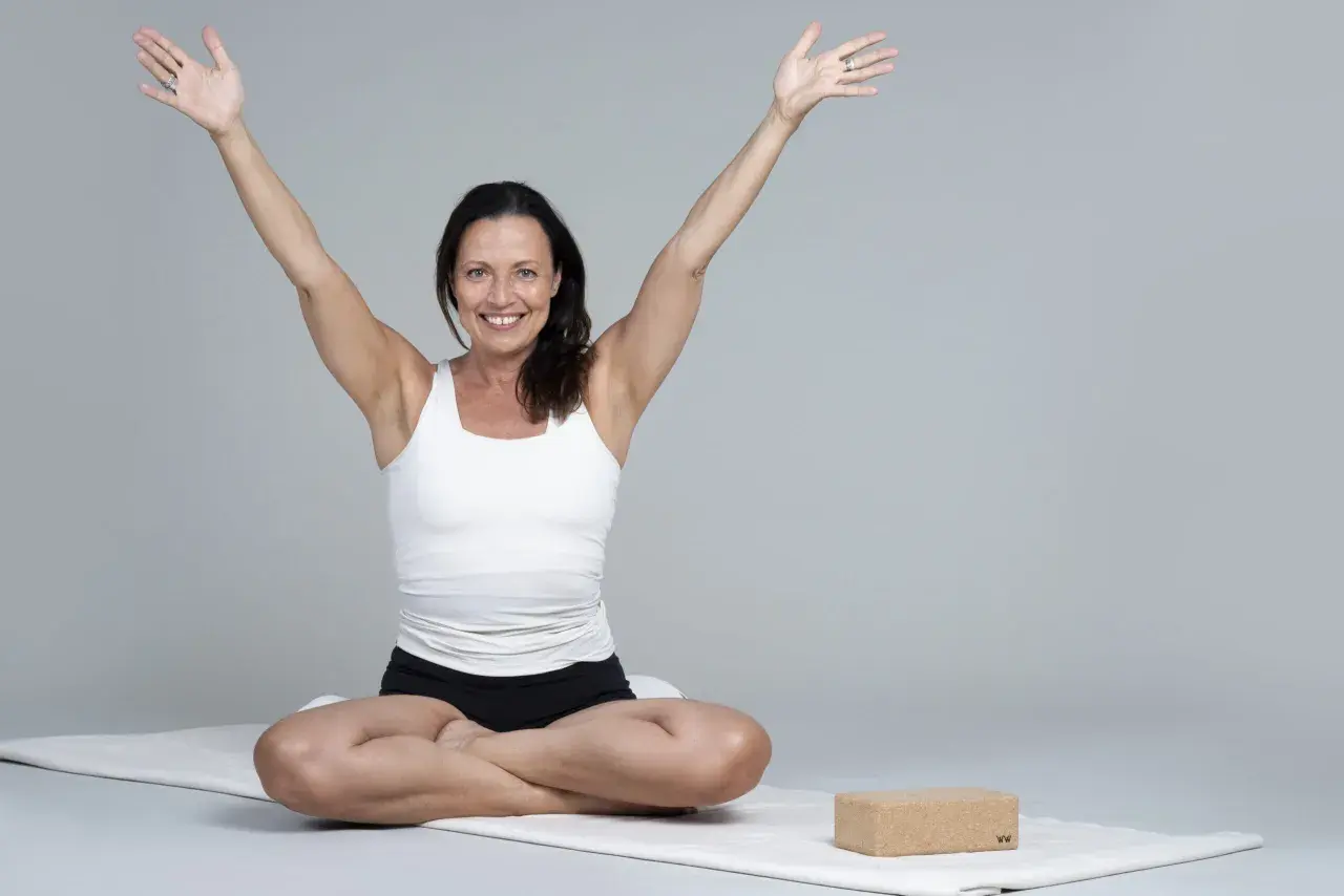Kvinna i meditationsställning med armarna uppåt, utstrålar lugn och glädje. Hon praktiserar metta meditation för inre frid.