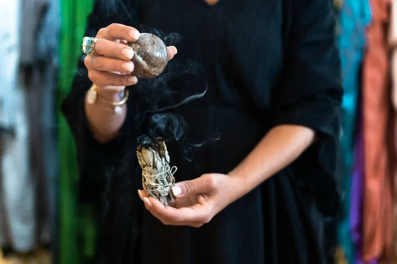 En person håller en rökande salviabunt och en sten. Rena kristaller kan ge energi till ritualen.