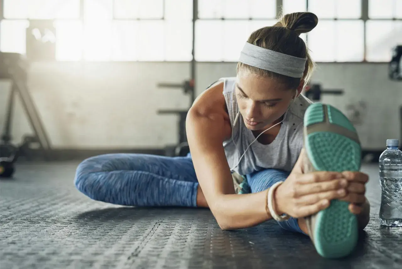Kvinna stretchar benet på gymgolvet, lyssnar på musik. En del av hennes fascia yoga-rutin.
