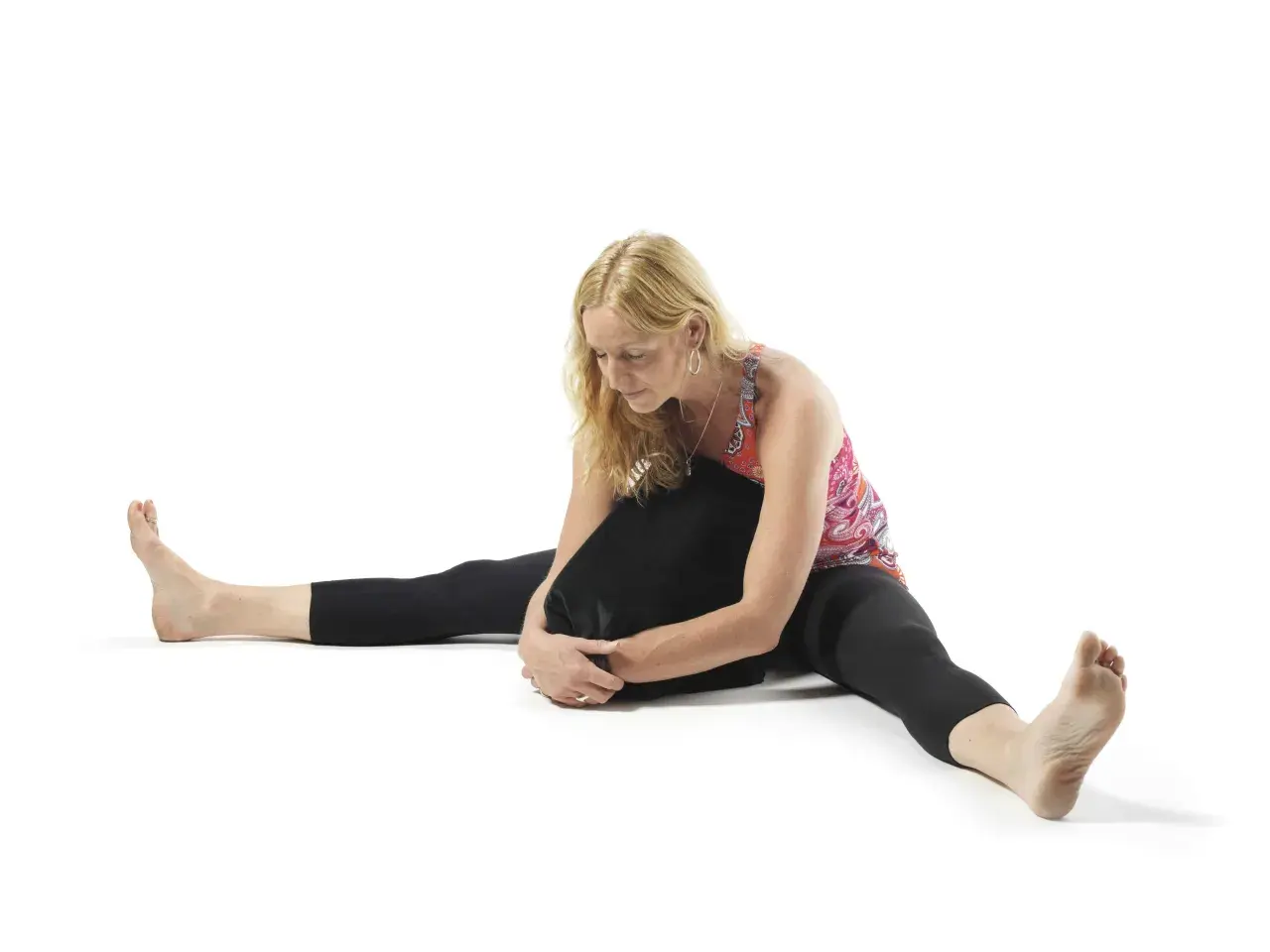 Kvinna i yin yoga-position med benen isär och en kudde mot bröstet. Utforska yin yoga effekter för ökad rörlighet och lugn.