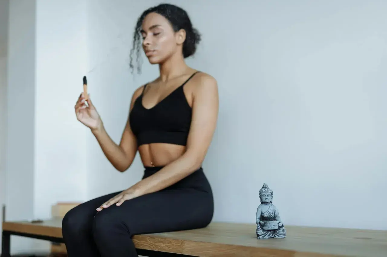 Kvinna med slutna ögon håller en rökelsepinne, en Buddha-statyett bredvid. Forskning om sa ta na ma meditation.