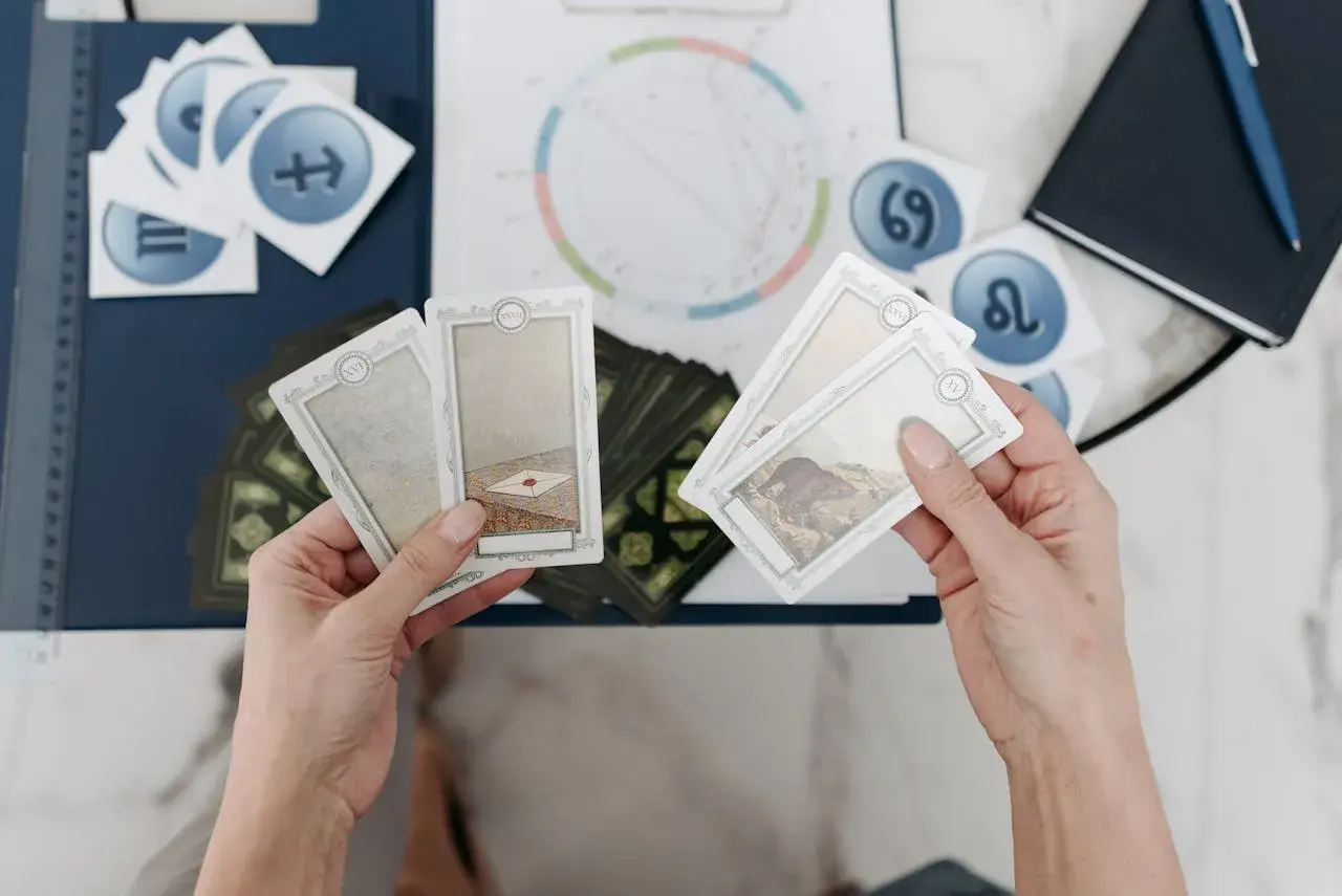 Händer håller tarotkort med symboler för sjunde huset astrologi. En astrologisk karta och stjärntecken syns i bakgrunden.