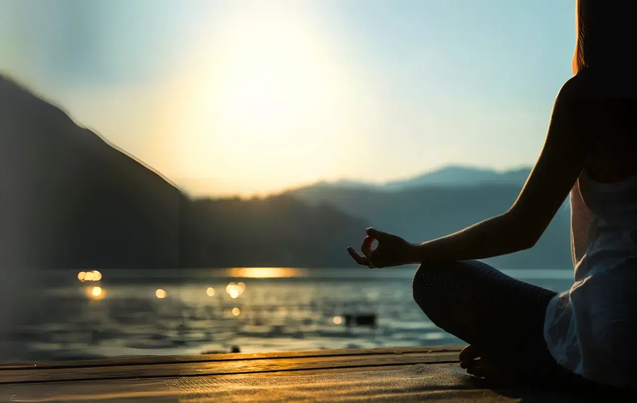 Person mediterar vid solnedgången, en lugn scen som kan inspirera till en ayurveda utbildning.