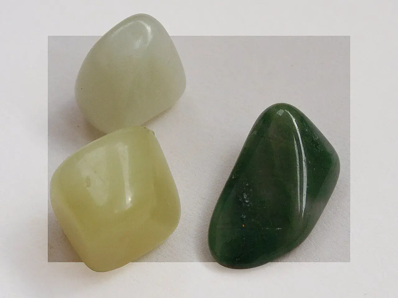 Three smooth, polished jade stones: one pale green, one light yellow-green, and one dark green.