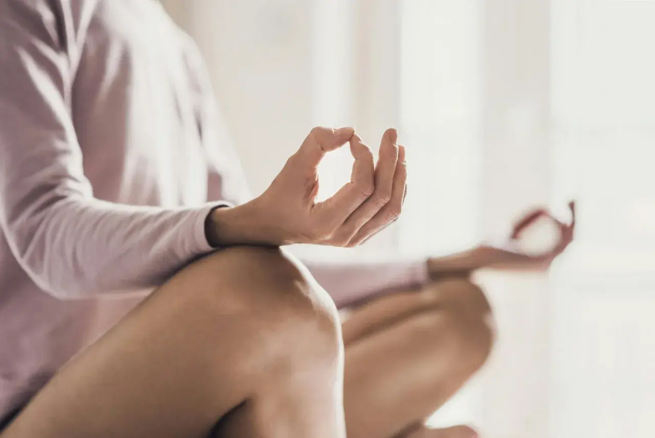 En person sitter i meditationsställning, med händerna i mudra. En bild som visar meditation effekter av lugn och ro.