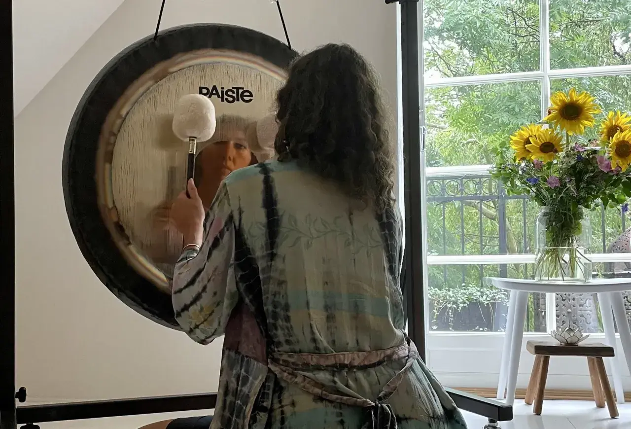 Person i färgglad kimono förbereder sig för gong bad. En stor gong står framför ett fönster med solrosor.