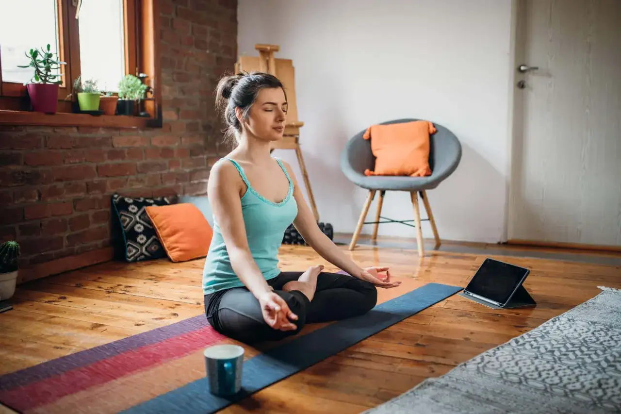 Kvinna med slutna &ouml;gon mediterar p&aring; en yogamatta, f&ouml;ljer en gratis yoga app p&aring; en surfplatta.