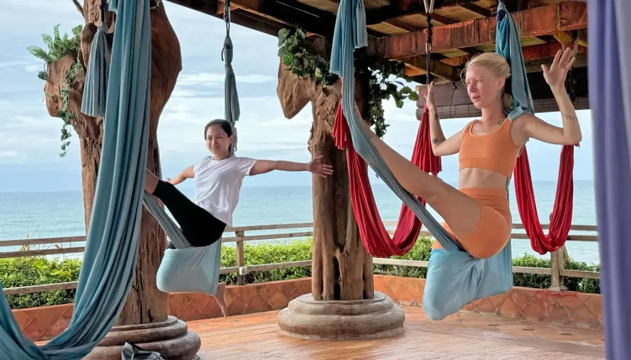 Tv&aring; kvinnor ut&ouml;var flying yoga i h&auml;ngmattor vid havet.