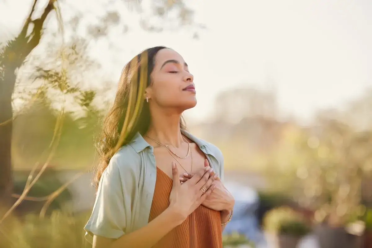 Kvinna med slutna &ouml;gon och h&auml;nderna &ouml;ver br&ouml;stet, utstr&aring;lar lugn under metta meditation i solnedg&aring;ngen.