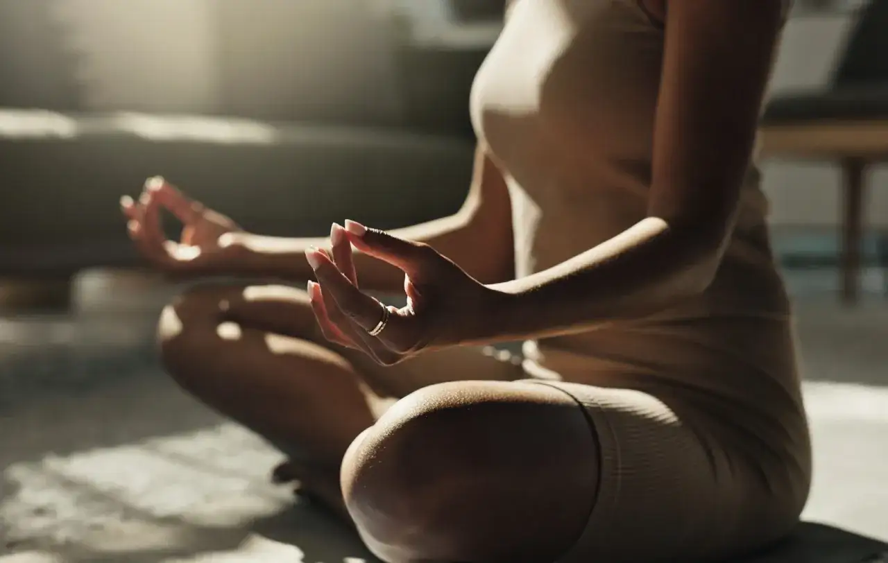 En person sitter i meditationsst&auml;llning, h&auml;nderna i mudra. Solstr&aring;lar lyser upp rummet och skapar en k&auml;nsla av mental avslappning.