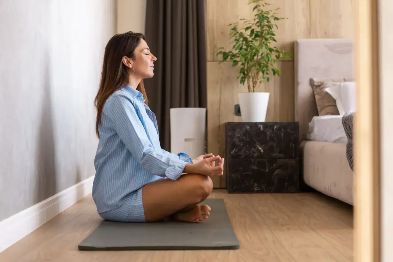 Kvinna med slutna &ouml;gon sitter i meditationsst&auml;llning p&aring; en matta. Hon upplever lugn och ro, en av m&aring;nga meditation effekter.