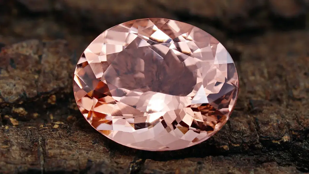En stor, fasetterad morganit &auml;delsten med rosa nyanser, som vilar p&aring; en grov, m&ouml;rk yta. Dess morganit egenskaper lyser i ljuset.