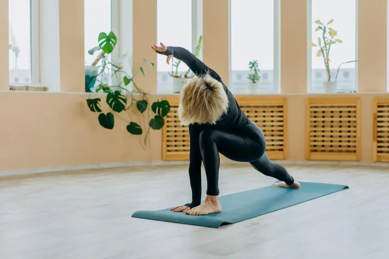 Kvinna i svart träningsklädsel utför en yogaövning på en blå matta. Hon sträcker ut armen över huvudet, en pose som främjar yoga avslappning.