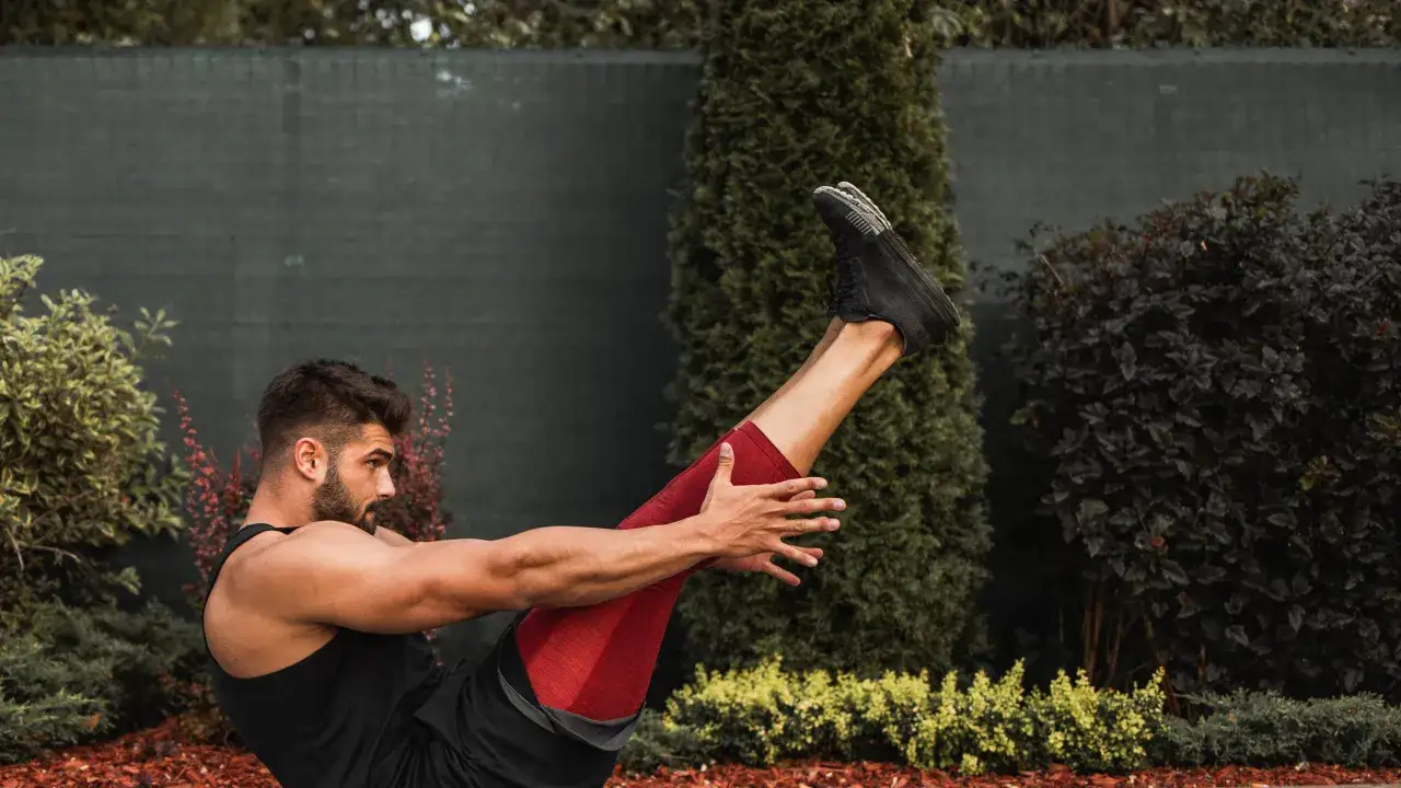 En stark yoga man tränar utomhus, med benen lyfta i en balanserad position.