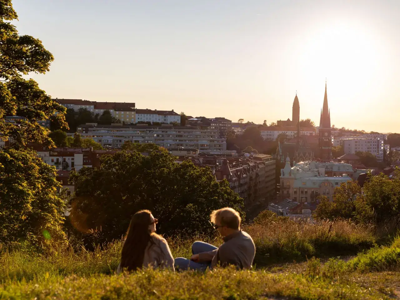 Tv&aring; personer njuter av solnedg&aring;ngen &ouml;ver en stad med kyrktorn, kanske en av Sveriges bl&aring; zoner.