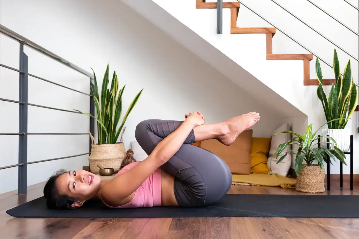 Kvinna utf&ouml;r yoga f&ouml;r att lindra diskbr&aring;ck. Hon ligger p&aring; rygg och drar kn&auml;na mot br&ouml;stet.