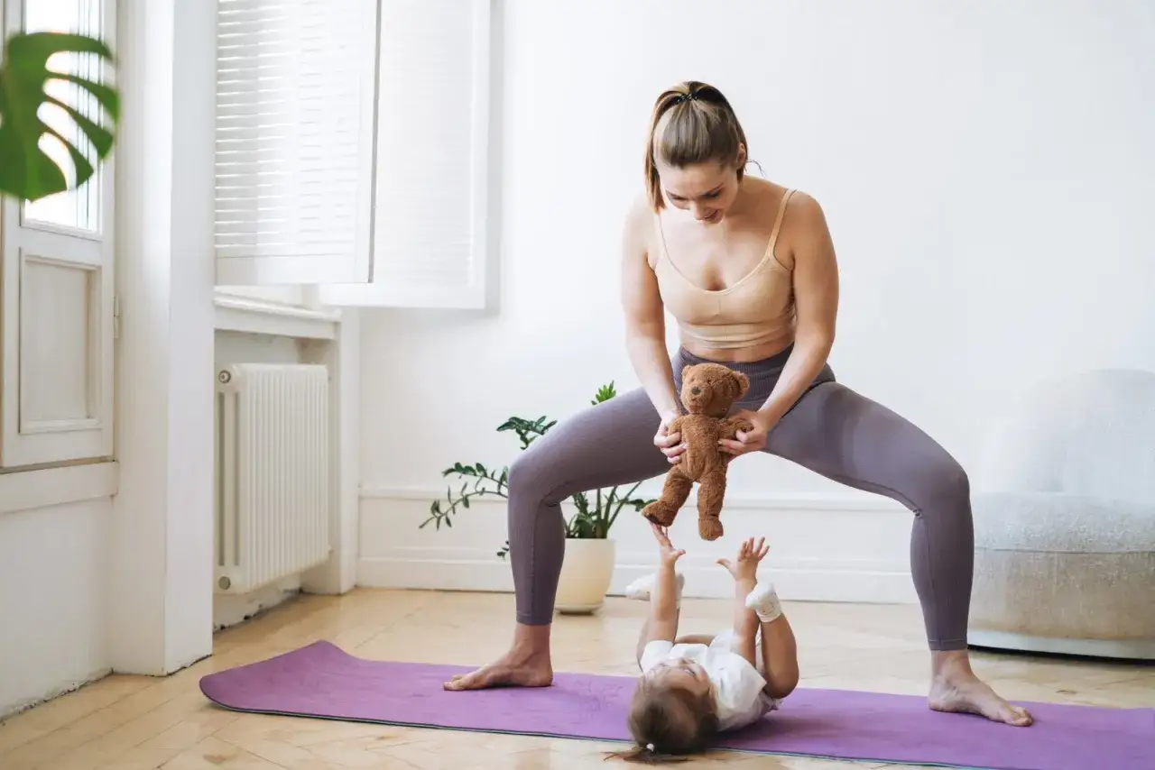 Mamma och barn leker baby yoga med en nalle.