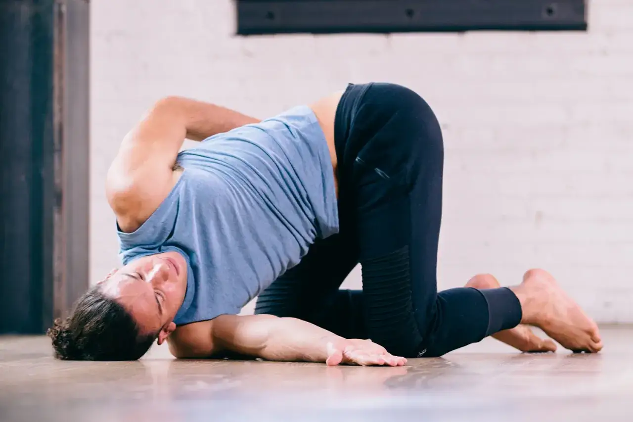 Man i blå tröja och svarta byxor utför en djup twist på golvet. En av många yin yoga effekter är ökad rörlighet.