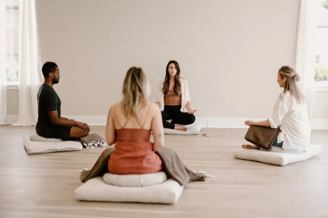 Jenny leder en mindfulness-session. Fyra personer sitter p&aring; kuddar i meditationsst&auml;llning i ett ljust rum.