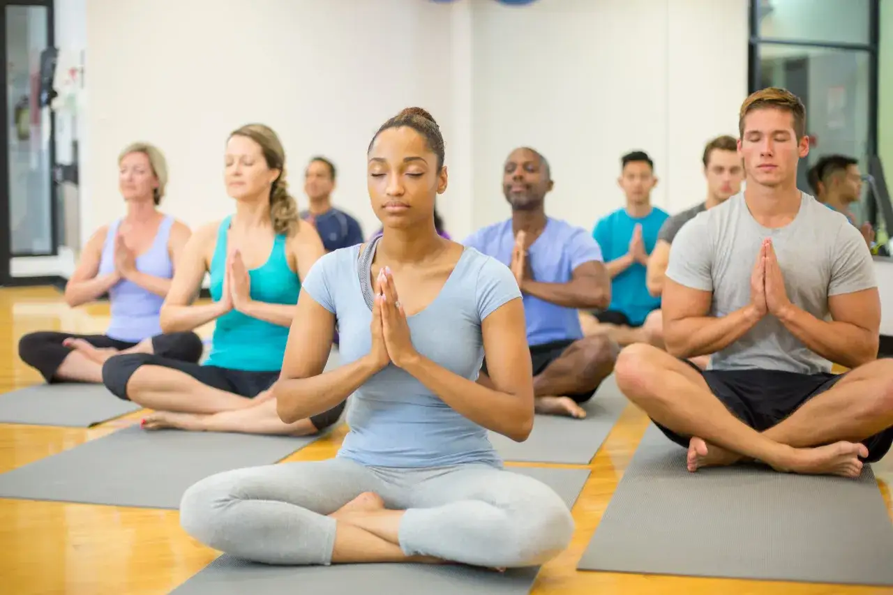 M&aring;nga m&auml;nniskor sitter p&aring; yogamattor i lotusst&auml;llning med slutna &ouml;gon, en del av en medicinsk yoga utbildning.