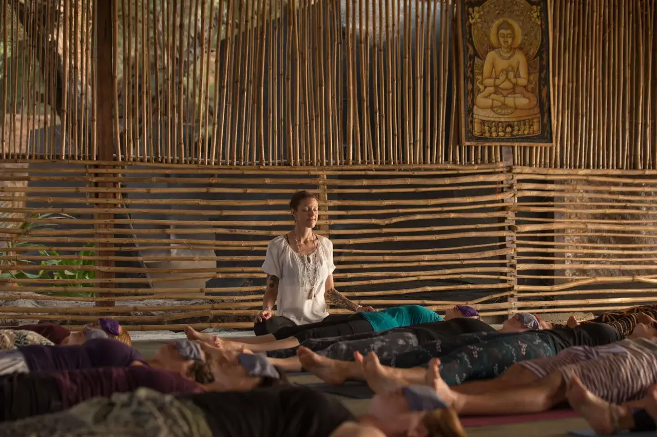 En kvinna leder en yoga nidra utbildning. Deltagare ligger p&aring; mattor med &ouml;gonbindlar, redo f&ouml;r djup avslappning.