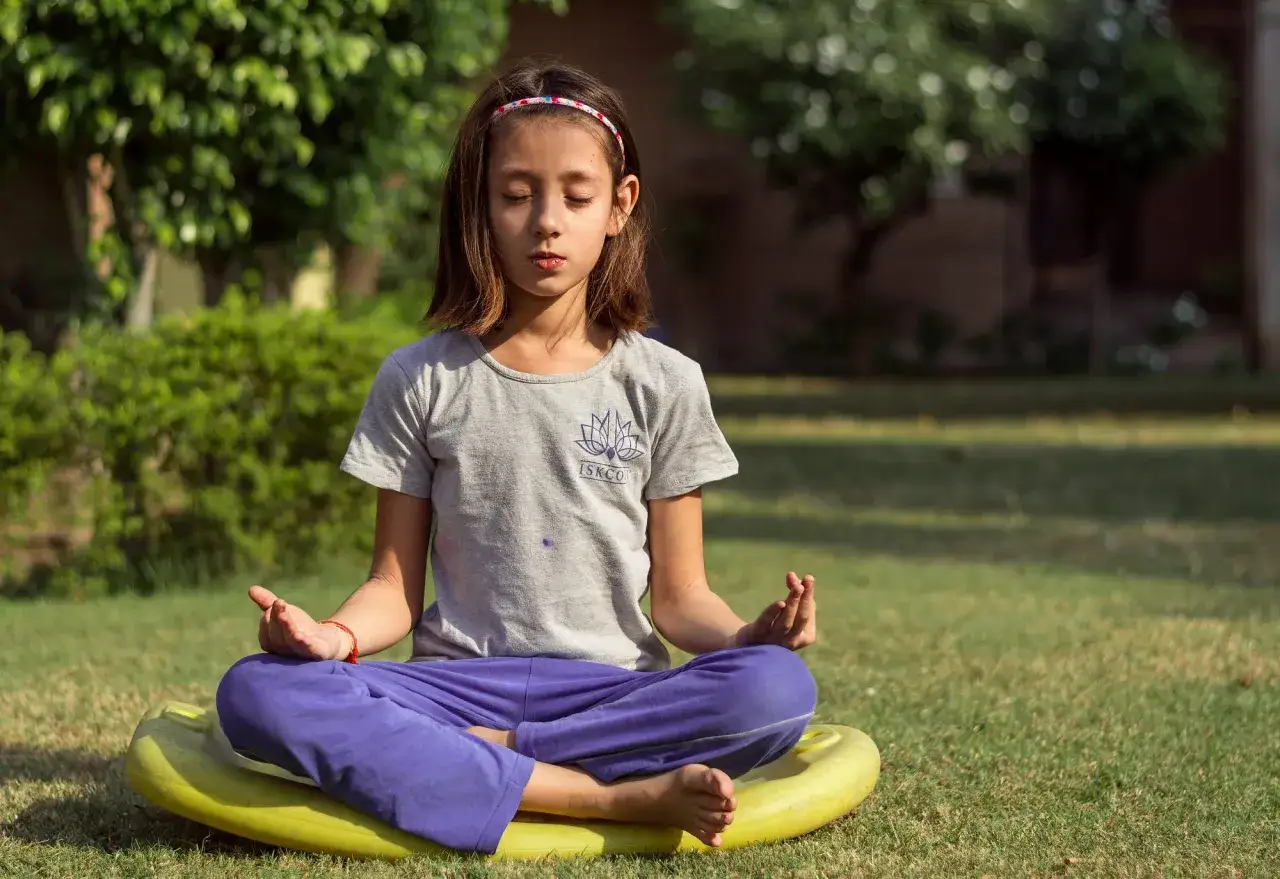 En flicka sitter i meditation utomhus, en lugn stund f&ouml;r en meditation barn.
