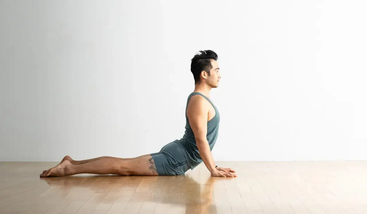 Man i yoga kobran, str&auml;cker ut ryggen p&aring; ett tr&auml;golv mot en vit v&auml;gg.